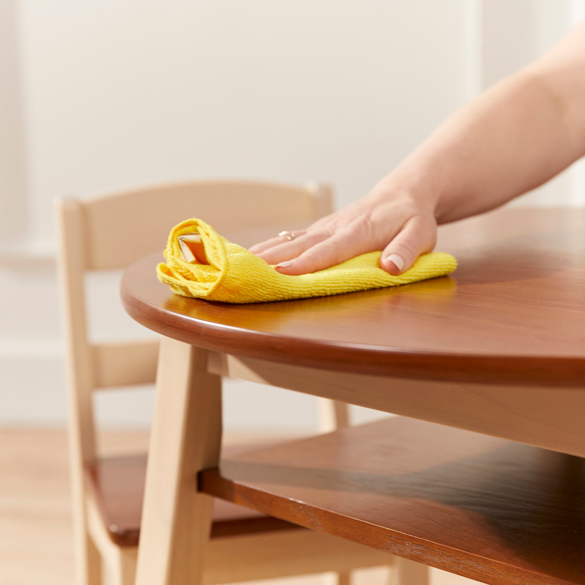 Round wooden table with natural wood chair in background, being cleaned with yellow cloth.