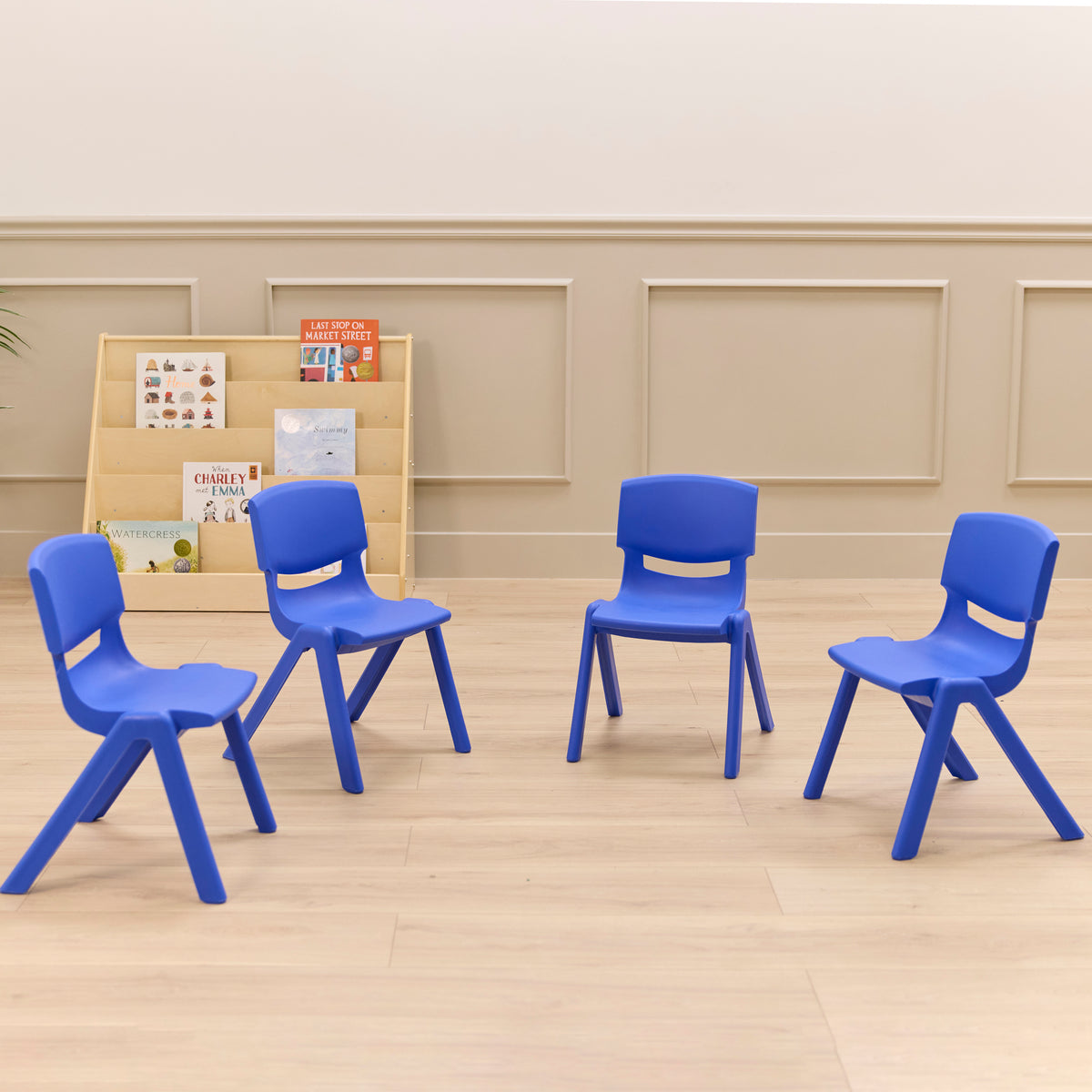 Four blue plastic children's chairs with curved backrests and angled legs arranged on a wooden floor.