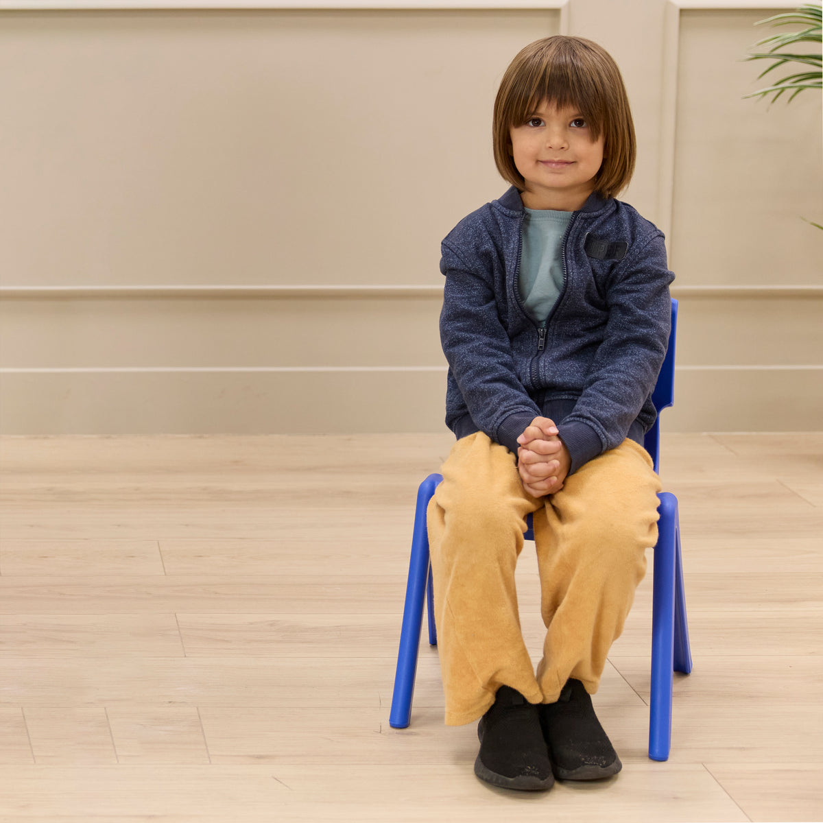 Child seated on blue stackable chair with 12-inch seat height in classroom setting.