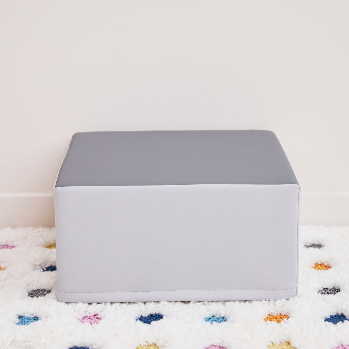 White rectangular pedestal with gray top surface, sitting on white textured mat with colorful spots.