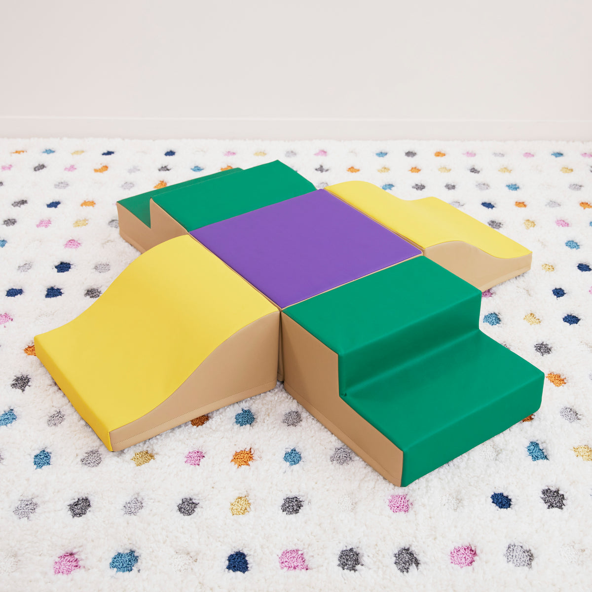 Tan and yellow foam climbing cube with dark top surface on colorful speckled mat.