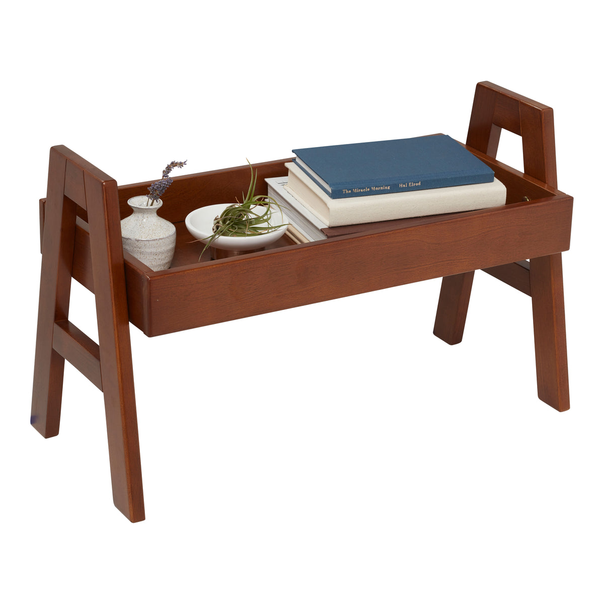 Brown wooden shelf organizer with raised sides holding books, a small plant, and decorative items.