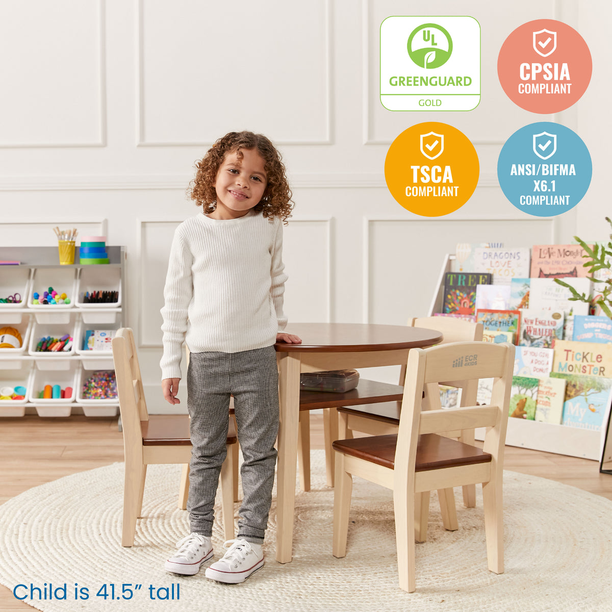 Child standing beside round wood table with brown top and two matching natural wood chairs with brown seats in playroom setti