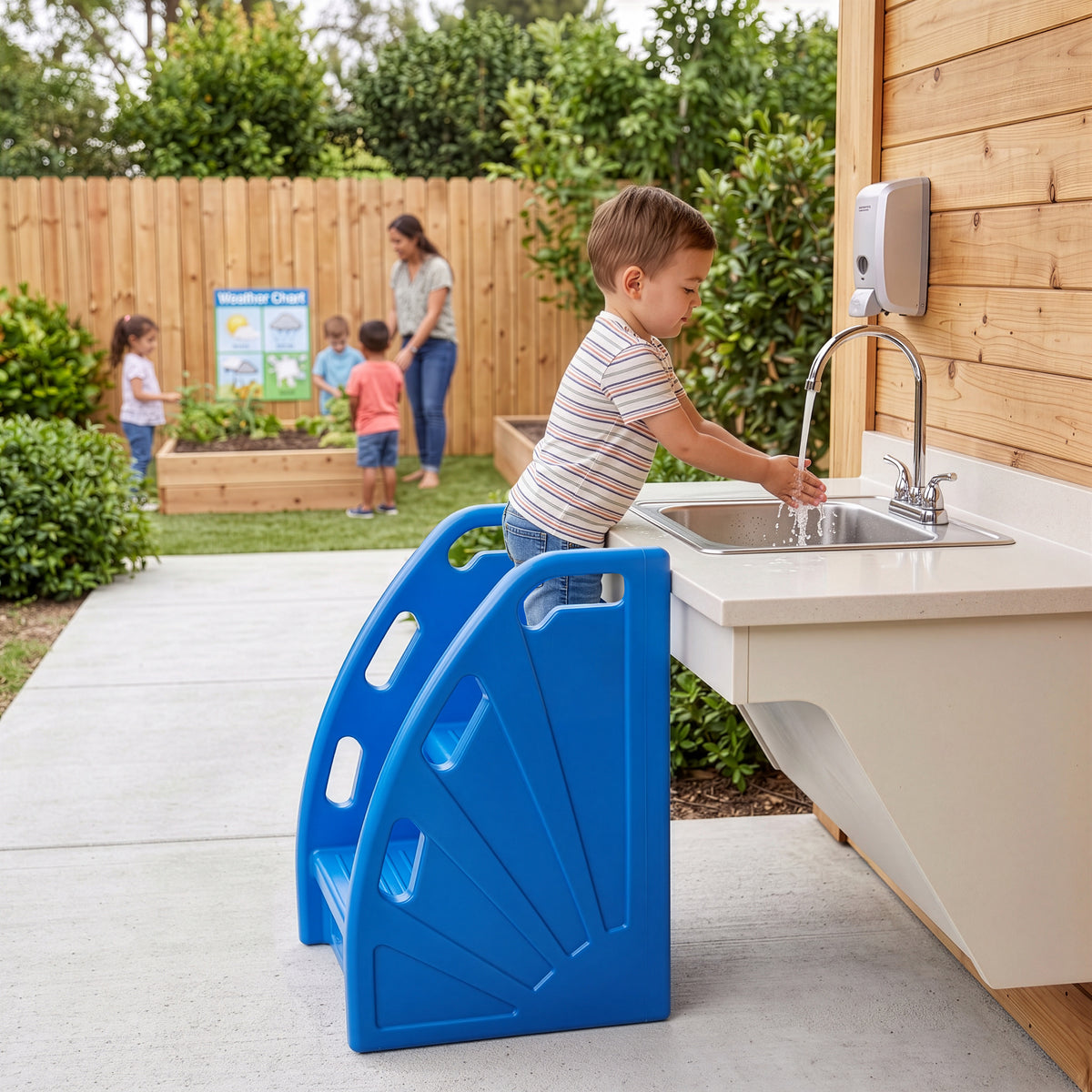 Blue plastic 2-step stool with handles being rinsed with water from a hose on pavement.