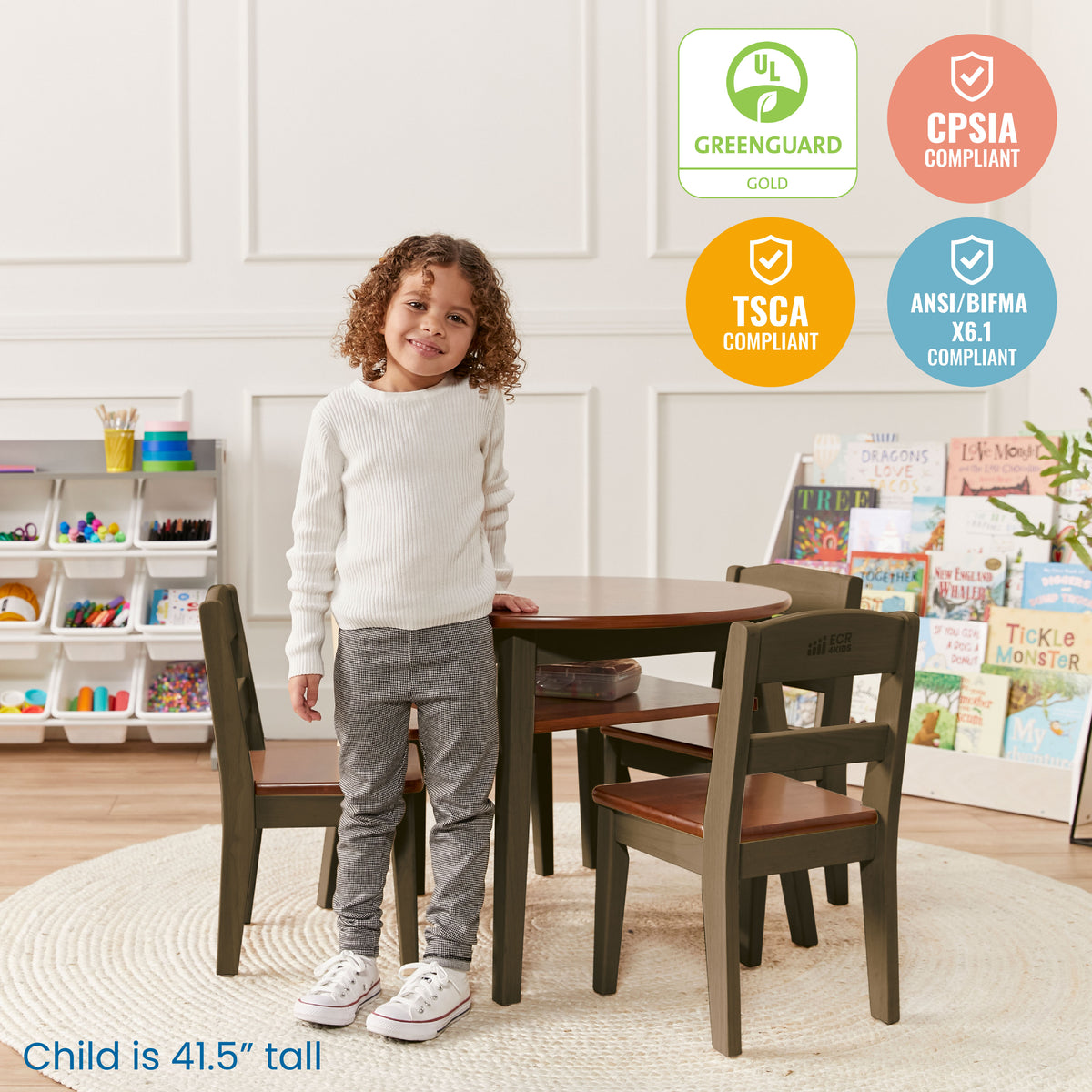 Child standing beside olive-green table with two matching chairs and storage shelf underneath, in playroom setting.
